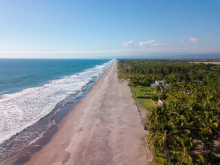Beautiful coastal aerial view of La Libertad beach with waves, beach houses and palm trees in El Salvador on a sunny day