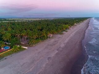 Aerial view of coastline of La Libertad in El Salvador with lush palms and tranquil waves at sunset purple limelight.