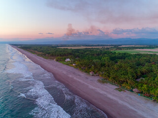 Aerial view of sunset over the quiet beaches of La Libertad in El Salvador with beach houses near the waves lapping on the shore