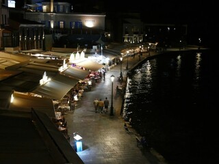 Tourists walking at night on the venetian harbour in Chania, Crete, Greece, between restaurants and the sea, enjoying the nightlife