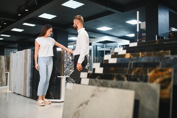 Young woman with sales man choosing tiles at building market