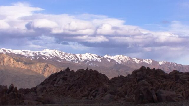 Pan shot of the Alabama Hills, in shadow, with the snow-capped Inyo Mountains and unsettled skies in the background.