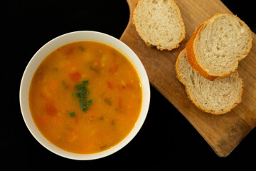 Sopa de legumes com caldo amarelo e fatias de pão para acompanhar. 