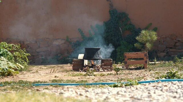 Traditional outdoor cooking in a large cauldron over a smoky campfire in a rural village backyard. An authentic scene of Anatolian countryside life and culture.