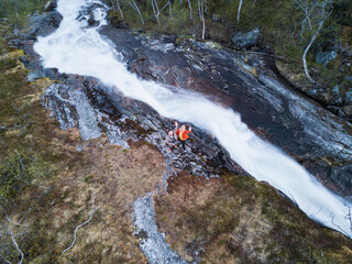 Greetings from wild Norway: a couple of travel bloggers stand on the rocks by a turbulent mountain...