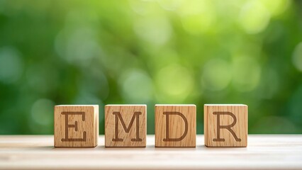 Letters EMDR on wooden blocks.  Eye Movement Desensitization and Reprocessing Psychotherapy Treatment concept. Blurred foliage in the background. Copy space.