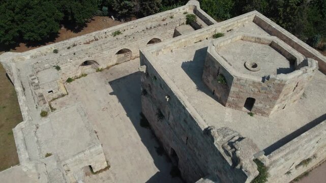 Aerial drone shot revealing the historic 'Jinn Tower' (Cin Kulesi) fortress in Payas, Turkey. The camera pulls back to show the Mediterranean Sea and harbor.