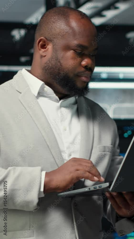 Poster vertical video technician walking in data center, using laptop to check hardware for system stabilit