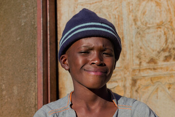 village single african boy sited in front of the house , in the yard, sunny day,