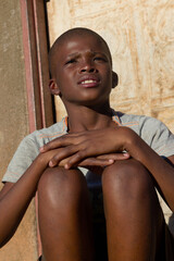 village single african boy sited in front of the house , in the yard, sunny day,