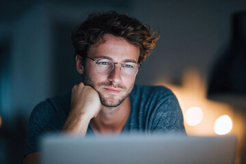 Focused young man in glasses working late on a laptop. Could represent concentration, remote work, creative projects, or online learning. A modern, relatable image.