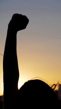 Defiant fist raised in protest against injustice: Silhouette of demonstrators hand against the fiery hues of a setting sun symbolizes resistance and hope.