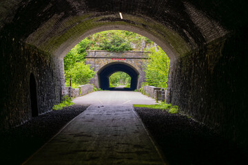 Obraz premium Long dark tunnel leading to a smaller tunnel and green trees in the background