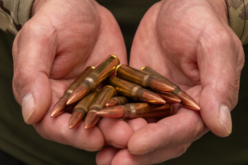 Obraz premium Male hands in military garb hold several large cartridges. The close-up symbolises the theme of war, weaponry, threat and self-defence.