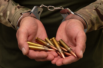 A man in military uniform with handcuffs on his wrists holds live ammunition in the palms of his...
