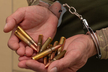 Handcuffed hands of a man in camouflage holding ammunition. The scene symbolises war crimes, illegal possession of ammunition.