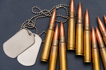 Military dog tags (soldier tags) and a few rifle cartridges lie on a dark textured surface.