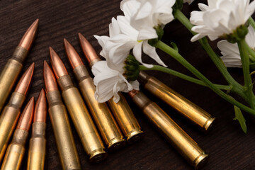 Flowers and bullets against a background of textured wood. The composition creates a powerful visual metaphor suitable for themes related to veterans, mourning, or the aftermath of war.