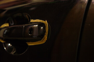 Close-up of the car door handle being polished, highlighting careful application of tape to protect...