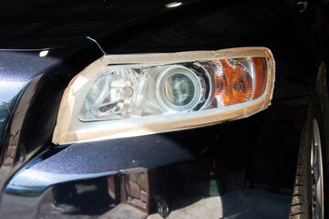Headlight is masked with tape during the car polishing process in a garage, showcasing meticulous...