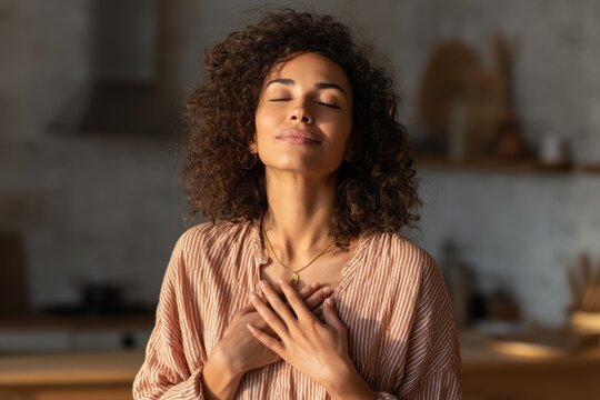 Calm woman meditating at home with hands on heart practicing mindfulness and focused breathing enjoying solitude and wellness