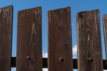 Fototapeta premium Close-up of weathered wooden fence planks against blue sky. Rustic texture and natural patterns of aged timber