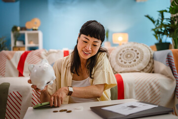happy mature japanese woman save money coins in the piggy bank at home