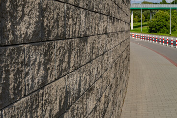Textured retaining wall along urban sidewalk with road and safety posts. Modern street architecture...