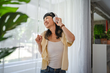 Playful japanese woman listen music on headphones and dancing at home