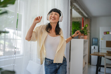 Playful japanese woman listen music on headphones and dancing at home