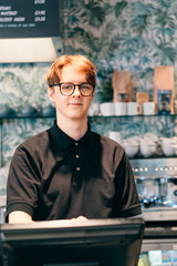 Young waiter serving customer at cash point in cafe. Man working with POS terminal. Cashier, barista checking for payment receipt. Hospitality, server and preparing a slip at the till in coffee shop.