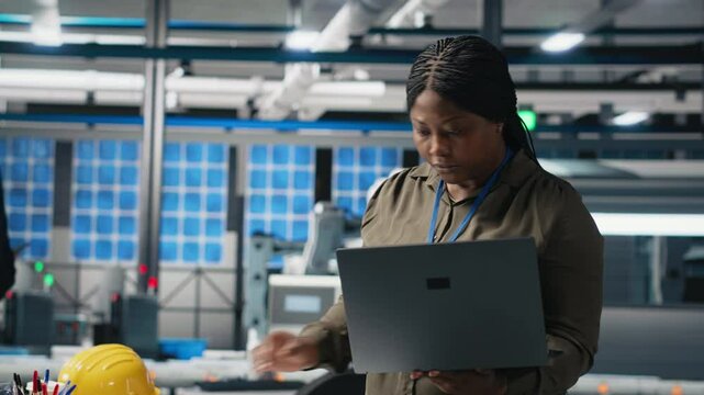 Woman master engineer examining production line for photovoltaics, reviewing manufacturing process data on laptop. Working on alternative energy success for industrial operations. Camera A.