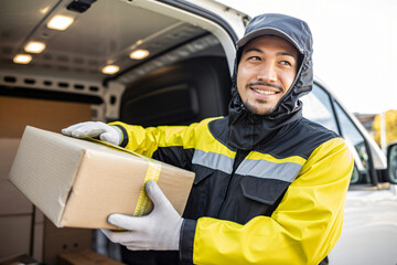 logistics worker loading parcels into delivery van while wearing protective rain gea