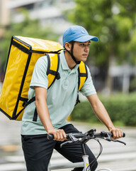 Obraz premium express delivery person cycling through light rain with insulated yellow delivery bag
