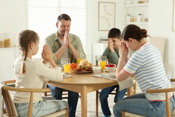 Family praying together before dinner at table indoors