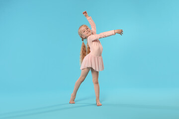 Fototapeta premium Cute little girl dancing on light blue background
