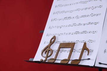 Stand with music sheets and wooden notes on red background, closeup. Space for text