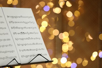 Note stand with music sheets against blurred lights, closeup. Space for text