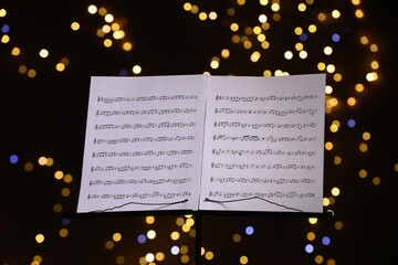 Note stand with music sheets against blurred lights, closeup. Bokeh effect