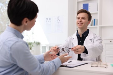 Ophthalmologist giving glasses to patient at white table in clinic