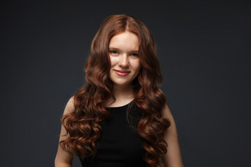 Fototapeta premium Portrait of beautiful teenage girl with healthy wavy hair on dark grey background