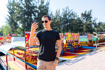 Hispanic Man Using Smartphone in Xochimilco with trajinera boats in the background, Mexico