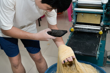 young asian man taking picture of raw homemade noodle
