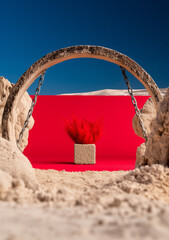 Red powder explosion from cube in desert and stone archway – geometric scene-setting installation art concept with surreal tension and abstract symbolic framing