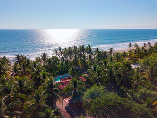 Aerial view of beach in El Salvador during daytime with palm tree line, pool and houses.