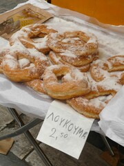 Traditional Greek loukoumades, coated in powdered sugar, displayed on white paper at a market stall...