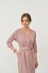 Elegant woman in mauve wrap dress with elbow-length sleeves, posing with hand on hip. Accessories...