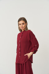 Woman in a stylish burgundy button-up blouse and matching pants, with a hand in her pocket. She has...