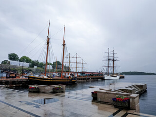 View of sailboats at a harbor in Oslo during a gray, rainy day. Calm water and overcast sky create a moody scene