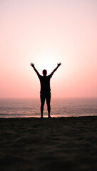 Man stretching with arms raised at sunrise on beach  
